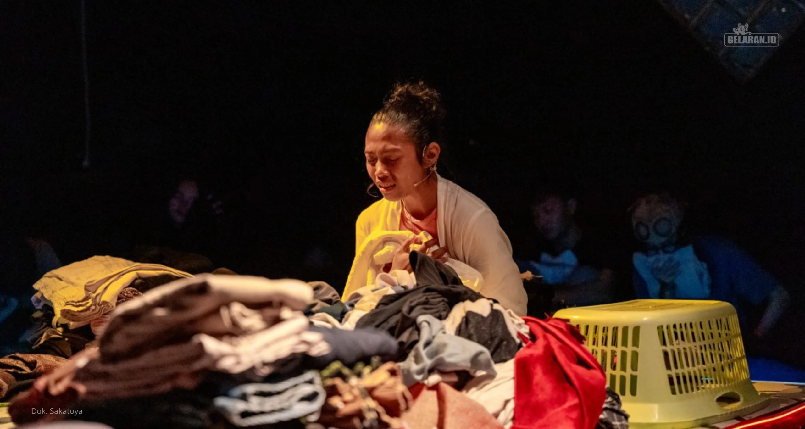 Performer memegang sehelai pakaian di antara tumpukan baju dalam sesi interaktif Mengurai Residu bersama Amalia Rizqi dan Ericha Nurcholifatin.