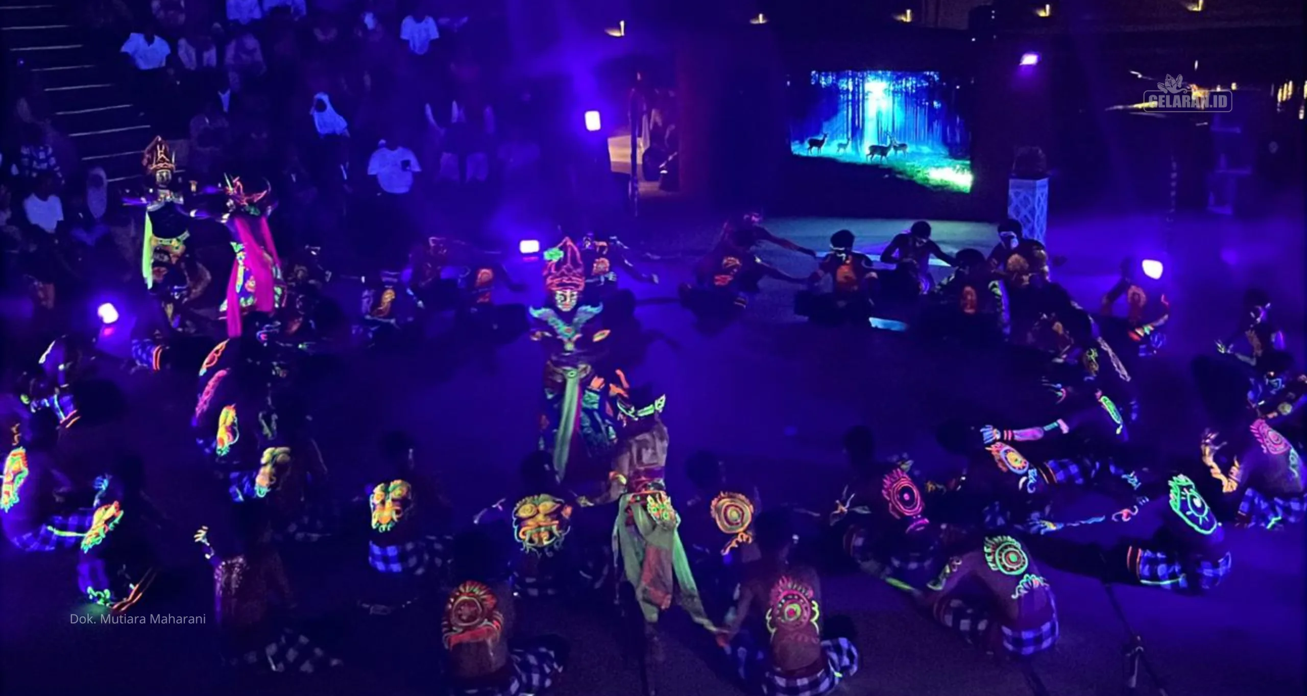 Pertunjukan Tari Kecak Glow in the Dark oleh Sanggar Pregina Agung di panggung Amfiteater TMII dengan 40 penari laki-laki membentuk lingkaran, tubuh dan wajah bercat neon menyala di bawah suasana malam, latar belakang danau Taman Mini Indonesia Indah.